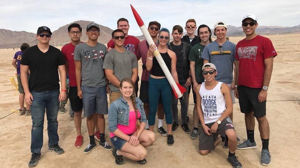A group of students holding up a model rocket in a large desert area